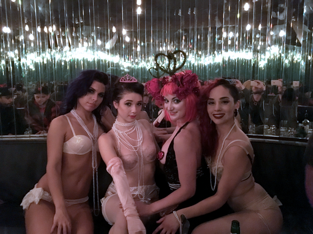 Three beautiful girls surrounding the Queen of Hearts in a mirrored VIP room